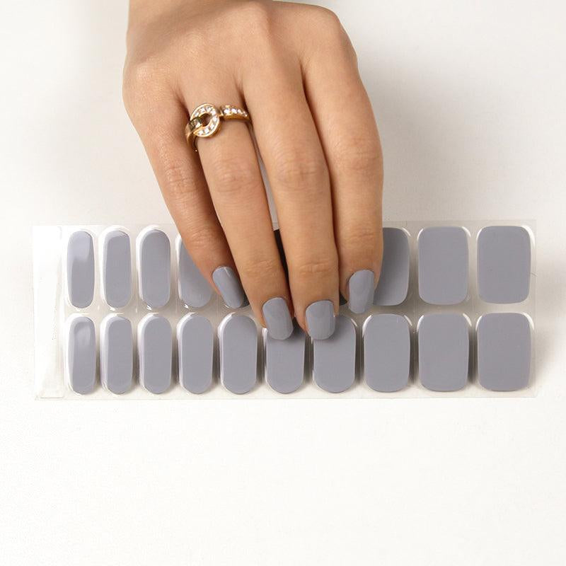 Sheet of storm gray stick-on gel nails with glossy finish on light skin tone, shown with nail strip sheet.
