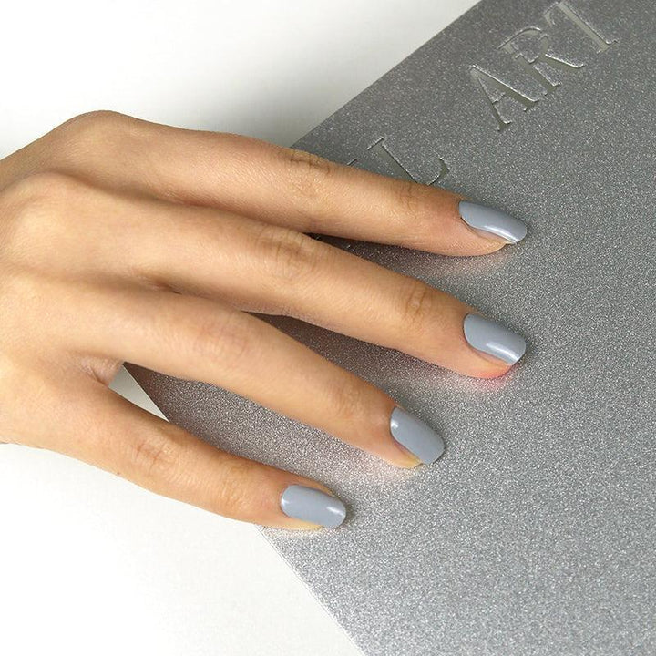 Glossy gray gel nail wraps on medium skin tone against silver textured background.