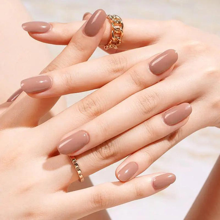 Taupe gel nail wraps with warm brown and rose undertones, creamy opaque finish on light skin tone, styled with gold rings in soft indoor light.
