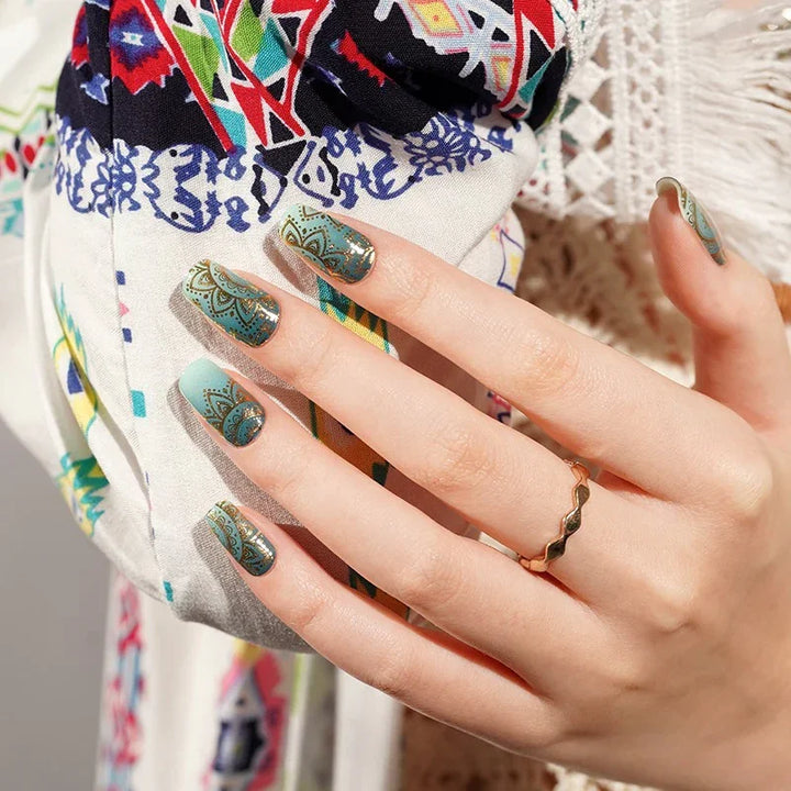Semi-cured gel nail wraps in teal ombre with gold mandala designs and glossy shine, shown on fair skin wearing gold jewelry and a patterned boho fabric.