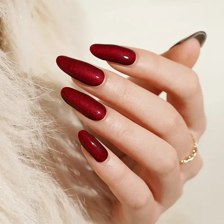Semi-cured gel nail wraps in bold red-wine tones with a cat-eye metallic sheen, shown on light skin wearing gold jewelry under warm light.