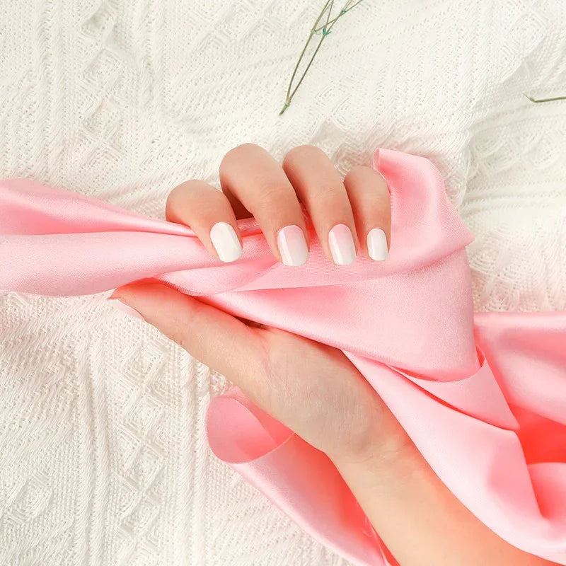 Hand wearing Baby Boomer gel nail wraps in a smooth white-to-pink gradient with a glossy glow, holding soft pink fabric.