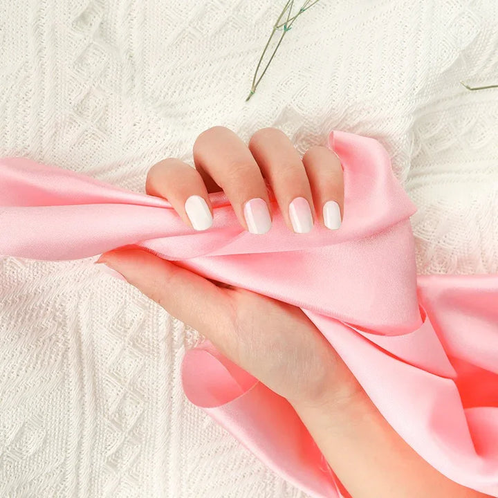 Hand wearing Baby Boomer gel nail wraps in a smooth white-to-pink gradient with a glossy glow, holding soft pink fabric.