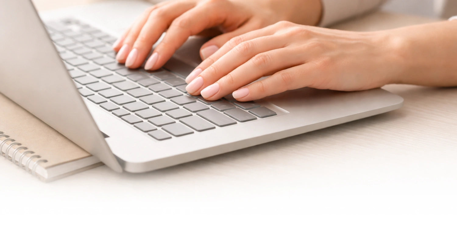 Hands typing on a laptop with soft pink gel nail wraps from the Gelly Back to Work edit