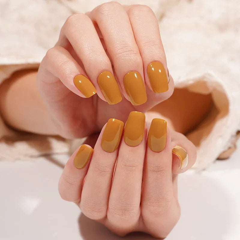 Light-skin hands featuring glossy burnt-caramel semi-cured gel nail stickers under soft studio lighting, shown against a cream textured sleeve.