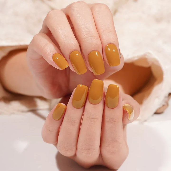 Light-skin hands featuring glossy burnt-caramel semi-cured gel nail stickers under soft studio lighting, shown against a cream textured sleeve.