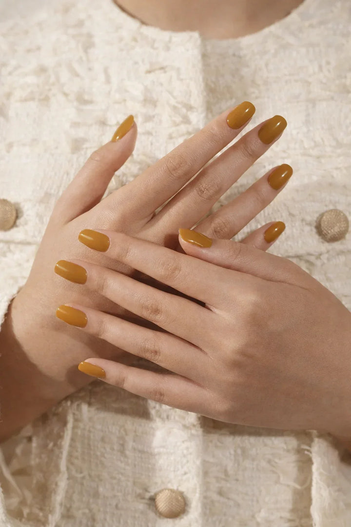 Medium light-skin hands wearing glossy burnt-caramel semi-cured gel nail stickers under soft studio lighting, paired a textured cream top.