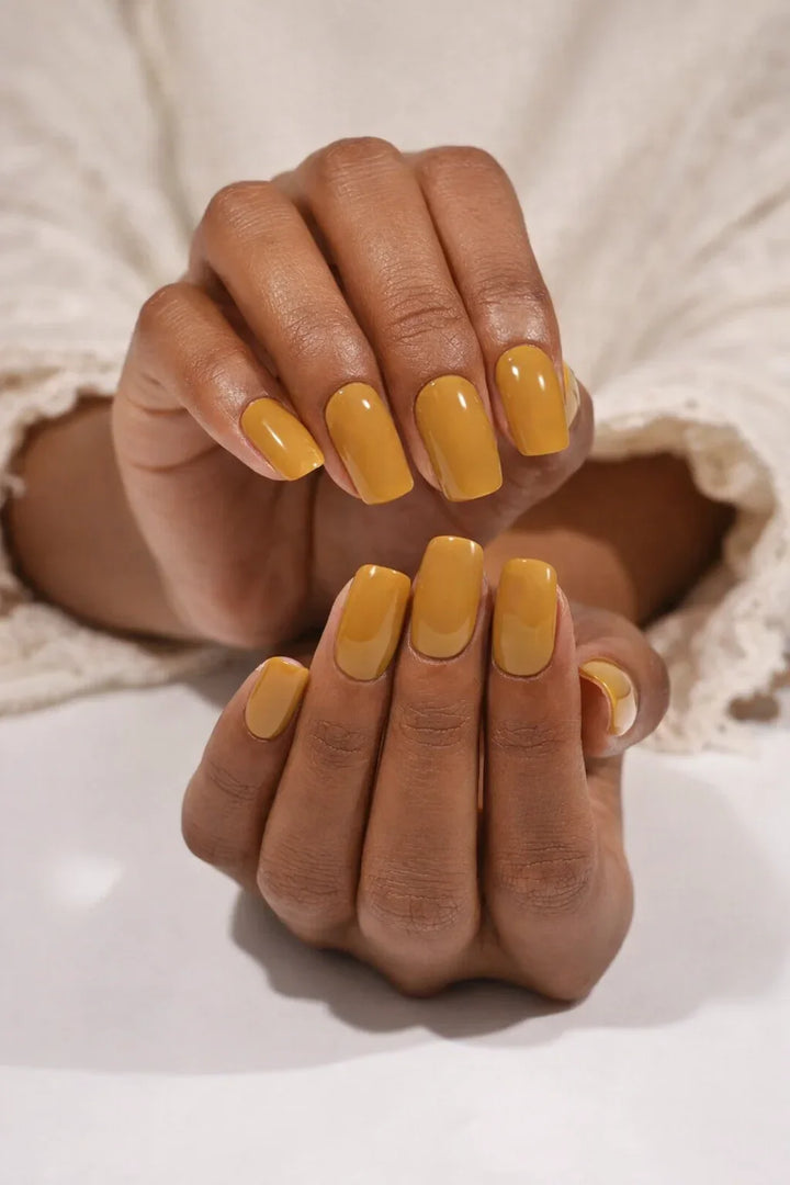 Medium-dark hands featuring glossy burnt-caramel semi-cured gel nail stickers under soft studio lighting, shown against a cream textured sleeve.