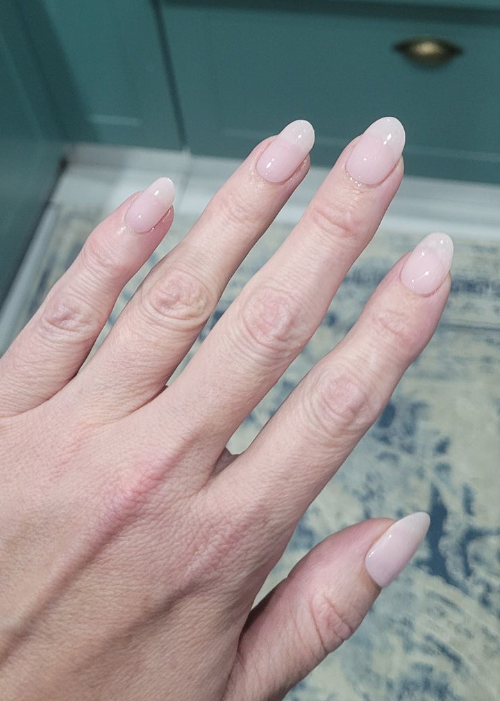Close-up of a hand with light pink nail polish against a teal cabinet background