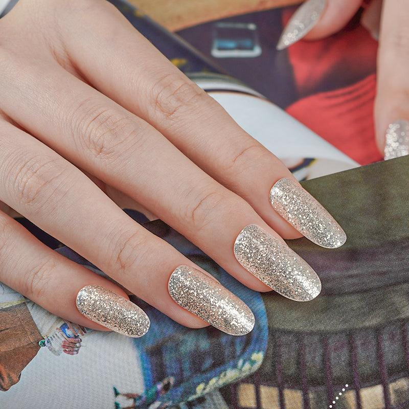 Champagne pale gold glitter gel nail wraps with dense sparkle and high-gloss finish on light skin tone, photographed under soft indoor lighting.
