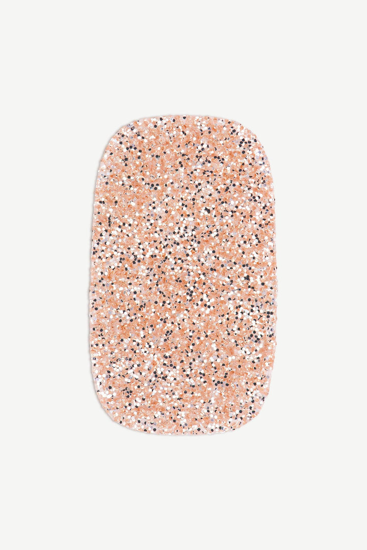 Macro image of a stick-on gel nail with champagne gold glitter and glossy finish, shown on white background.