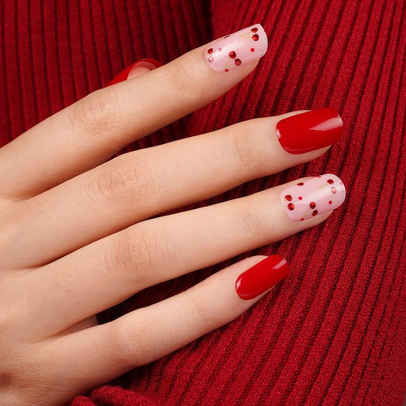 Cherry red and soft pink gel nail wraps with glossy finish and tiny red dot accents on light skin tone, styled against textured red knit fabric.