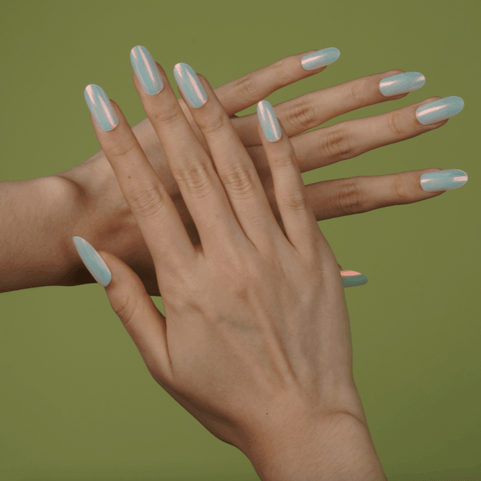 Stick-on gel nails in chrome mint with glossy iridescent finish on medium skin tone, catching light in soft indoor glow.