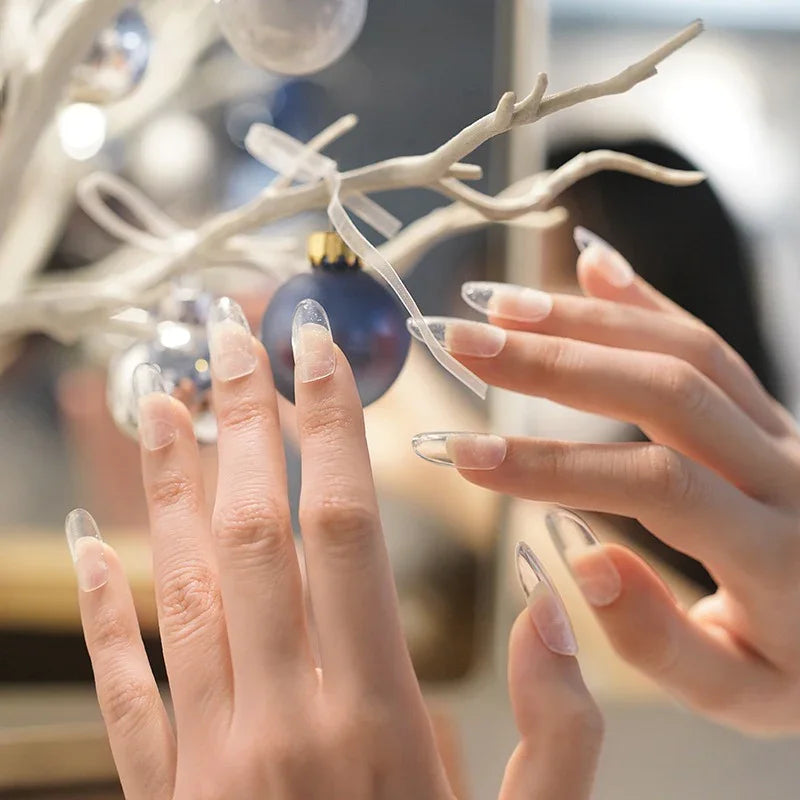 Hands wearing Clear Cat Eye gel nail wraps reflecting light with a delicate cat-eye shimmer and glossy finish, shown near a modern light fixture.
