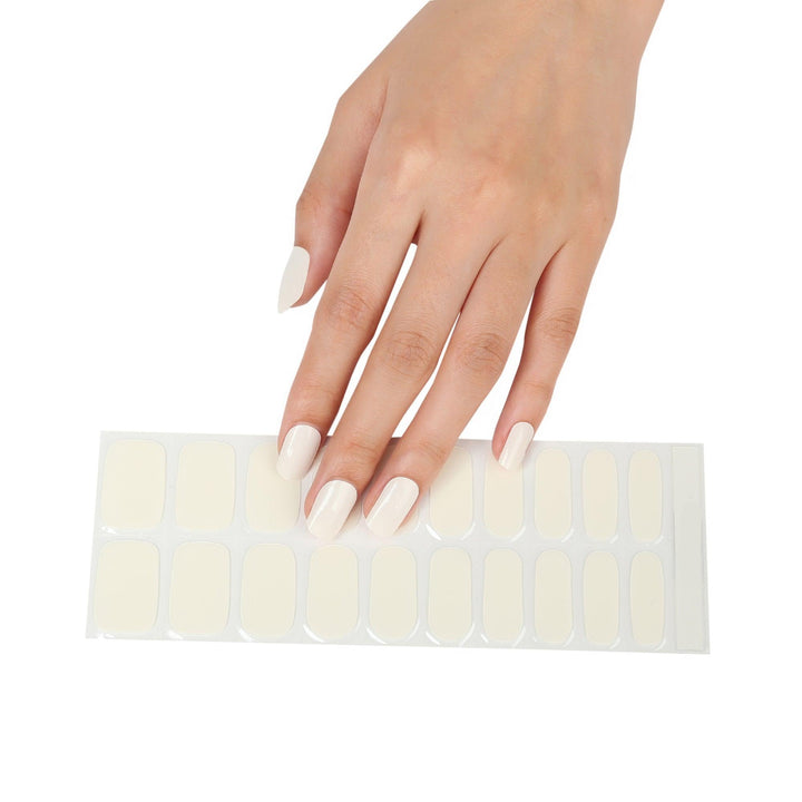 Sheet of off-white semi-cured gel nail strips with smooth milky tone and high-gloss finish, photographed on light background.
