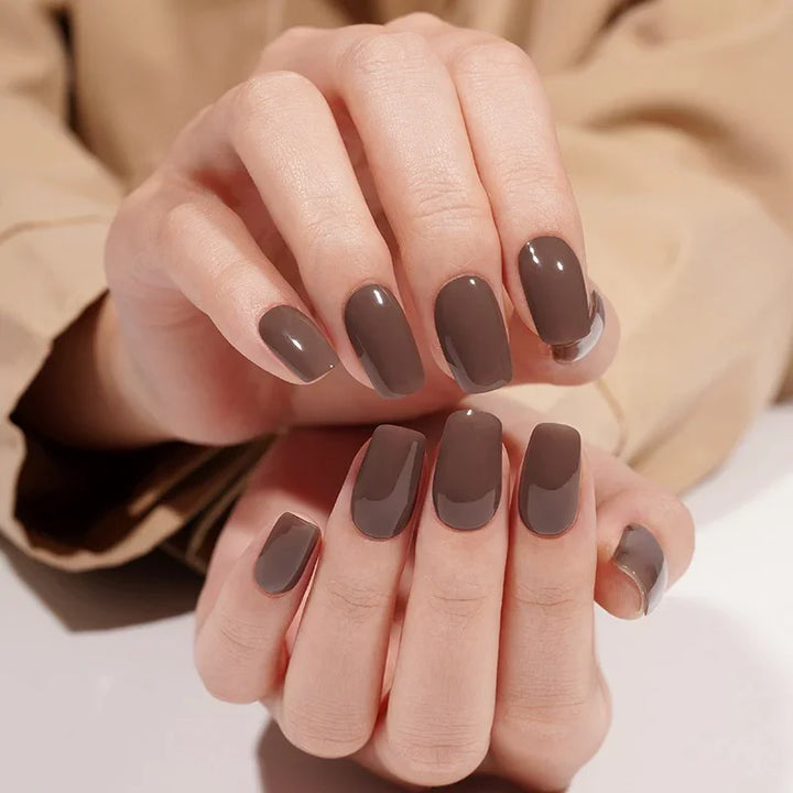 Dark Truffle semi-cured gel nail stickers in a rich chocolate-brown shade with a high-gloss finish, photographed under bright diffused studio lighting on light skin with a beige jacket in the background.