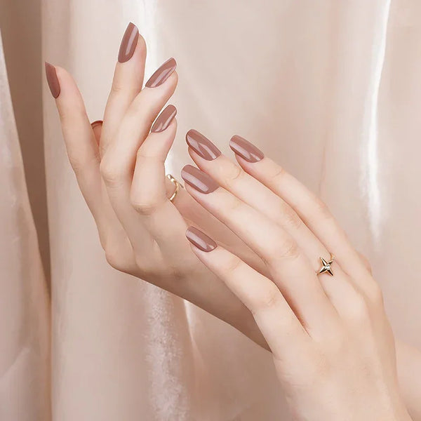 Hands wearing Dusk gel nail wraps in a muted rose-brown mocha shade with a semi-transparent, high-shine finish, shown against a silky neutral backdrop.