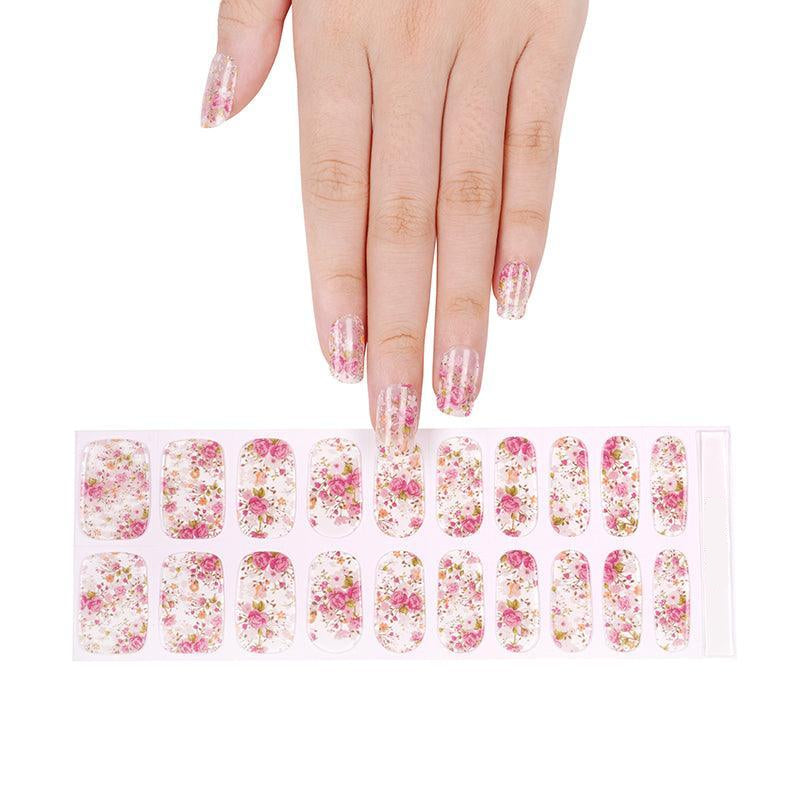 Sheet of sheer floral gel nail strips with pink, coral, and green print and glossy finish, held against light background.