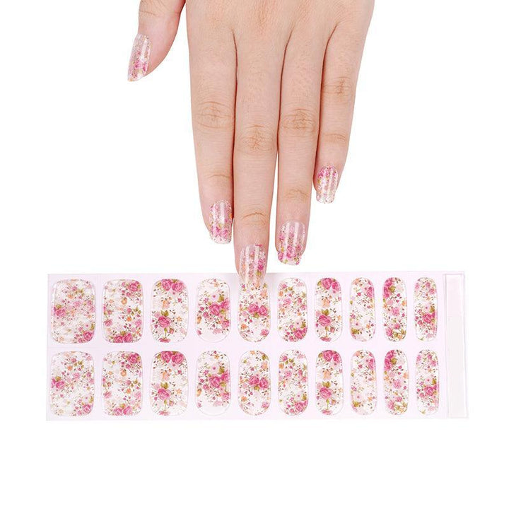 Sheet of sheer floral gel nail strips with pink, coral, and green print and glossy finish, held against light background.