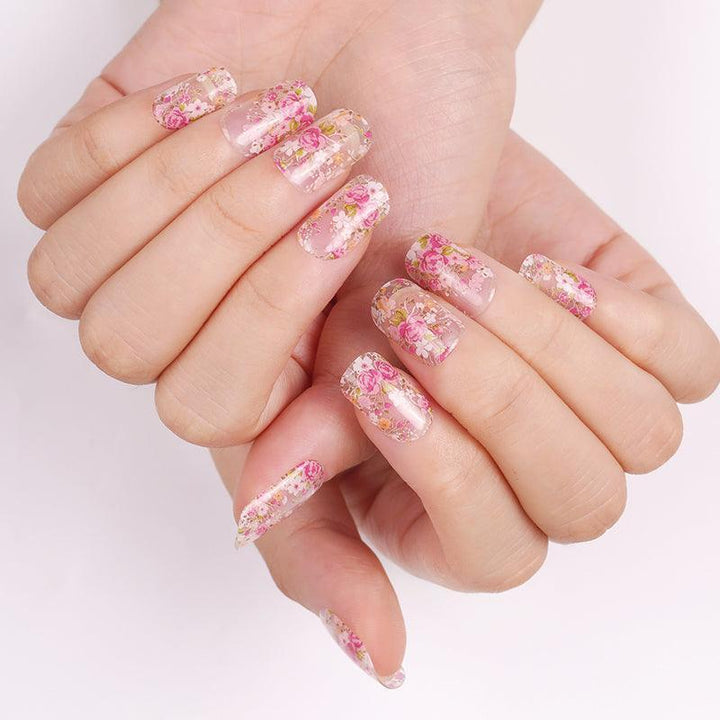 Transparent floral gel nail stickers with pink and coral blossoms on light skin tone, glossy finish photographed in diffuse lighting.