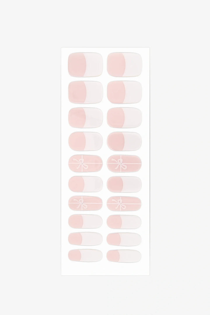 Sheet of semi-cured gel nail wraps with white-tipped and bow designs on translucent pink strips.