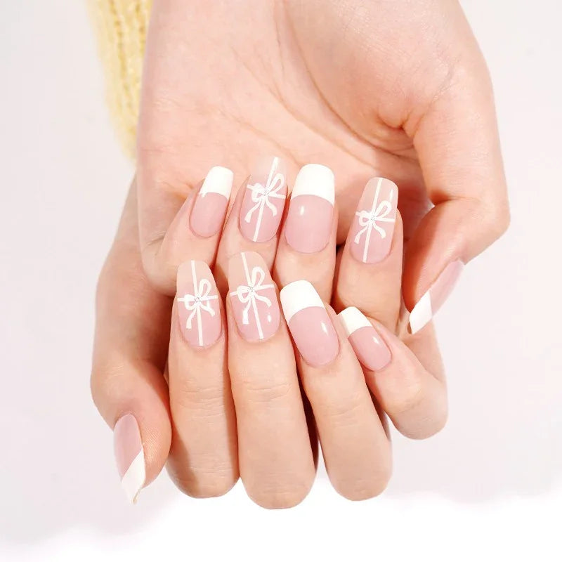 Close-up of manicured nails with French tips and small white bows, light pink base and glossy finish.