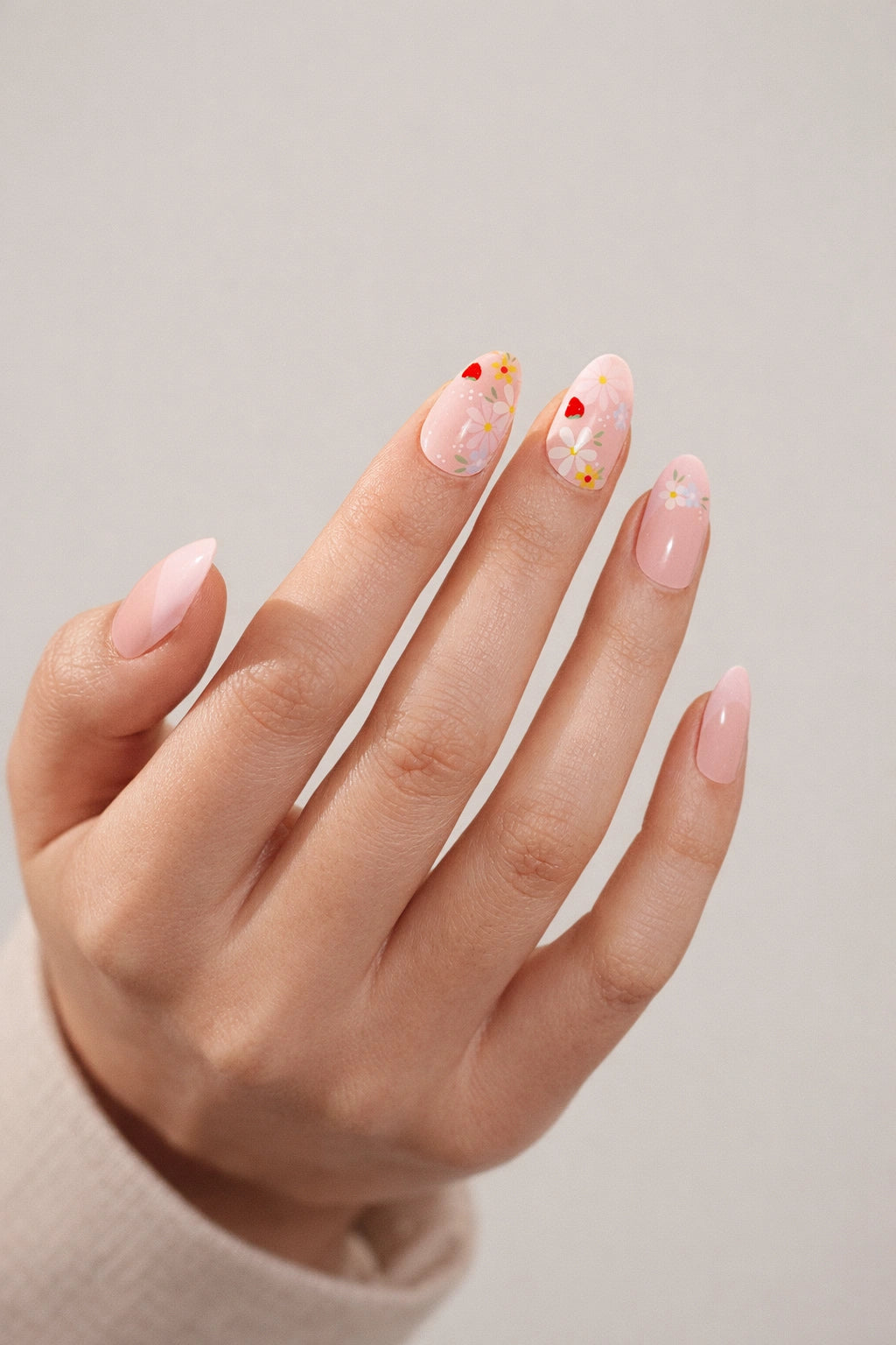 French Bloom semi-cured gel nail stickers, featuring a semi-sheer light pink blush base with soft French tips, delicate floral and strawberry accents on light skin, photographed under soft studio lighting with a cream knit long-sleeve outfit.