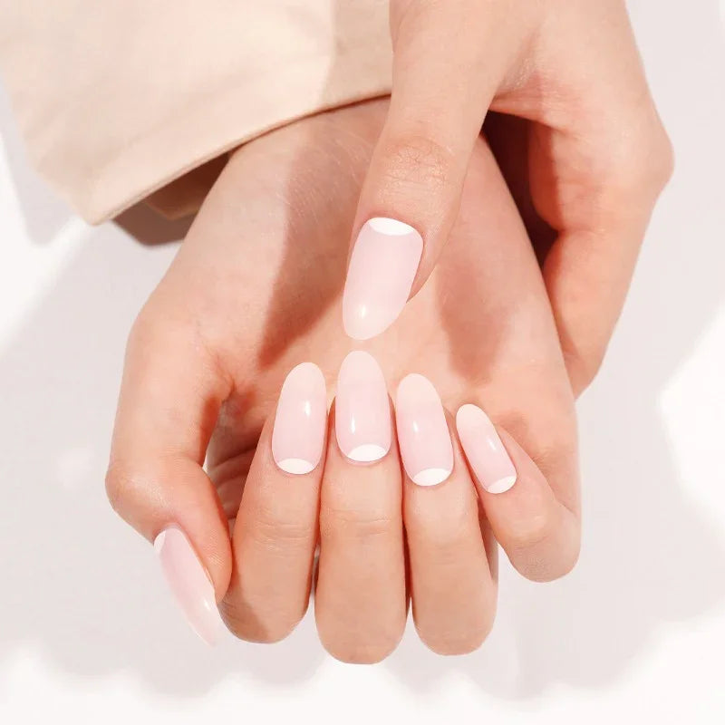 Two hands wearing French Moon semi-cured gel nail wraps — soft pink reverse-French manicure with natural glossy finish.