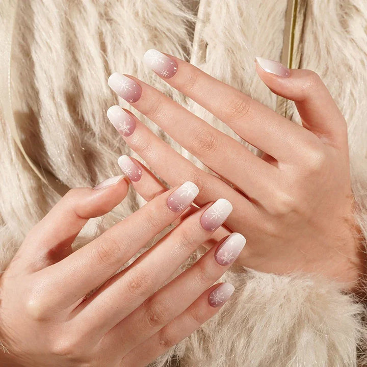 Frosted Boomer semi-cured gel nails in a soft mauve gradient with white snowflake accents, photographed under diffused studio lighting against light skin and a beige faux-fur coat.