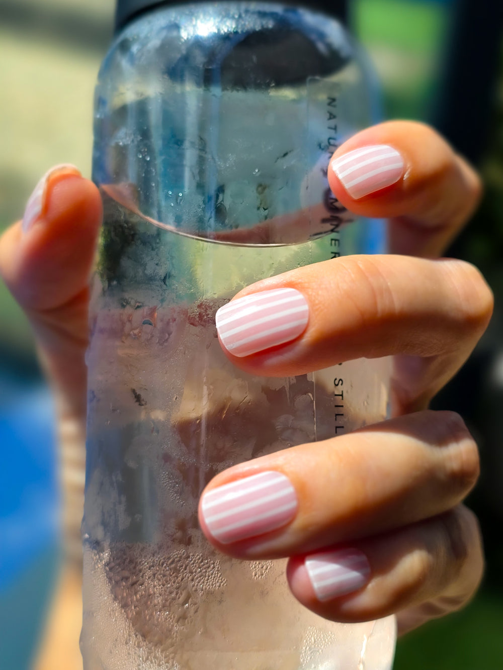 Hand holding a clear bottle with pink nail polish