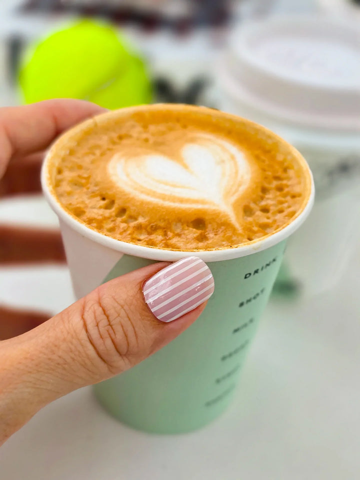 Hand holding a paper cup of cappuccino with a heart design on the foam.