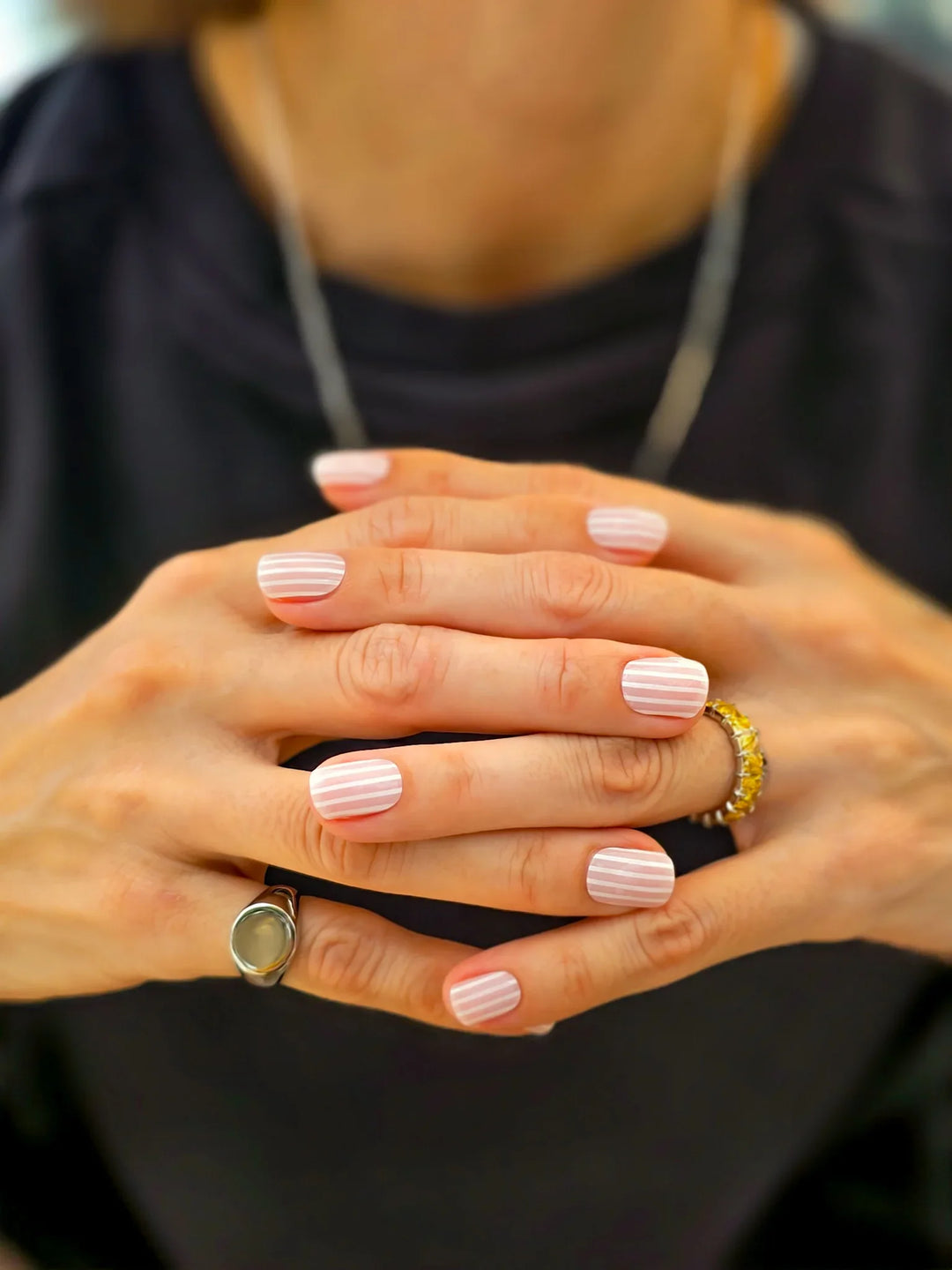 Close-up of hands with pink nail polish and rings on a blurred background