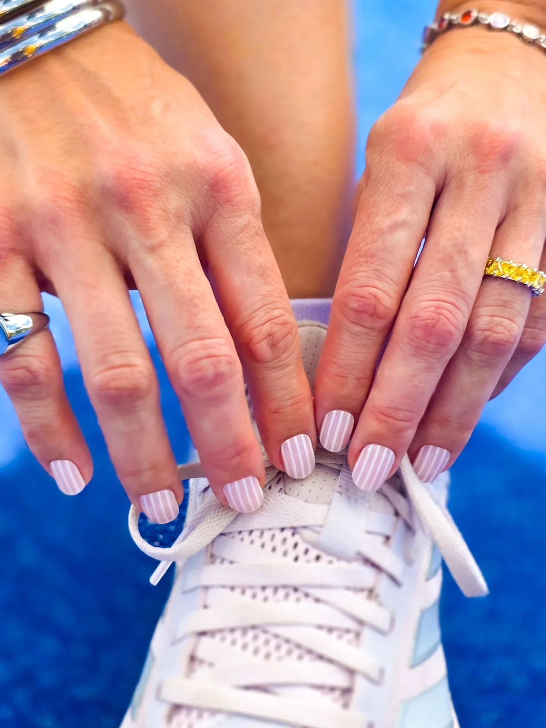 Close-up of hands with striped nail polish tying a white sneaker against a blue background