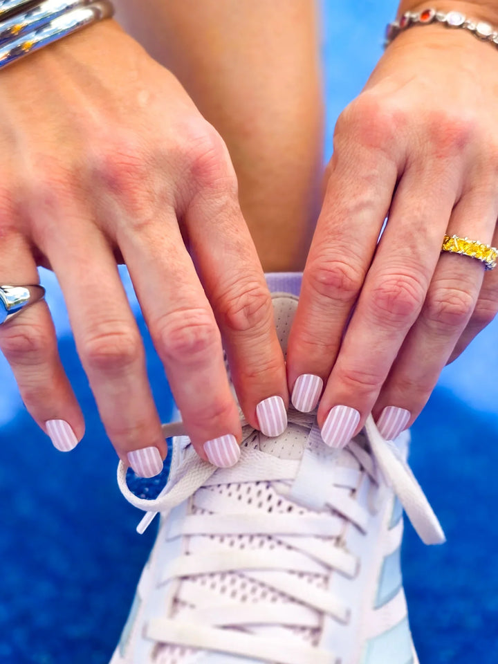 Close-up of hands with striped nail polish tying a white sneaker against a blue background