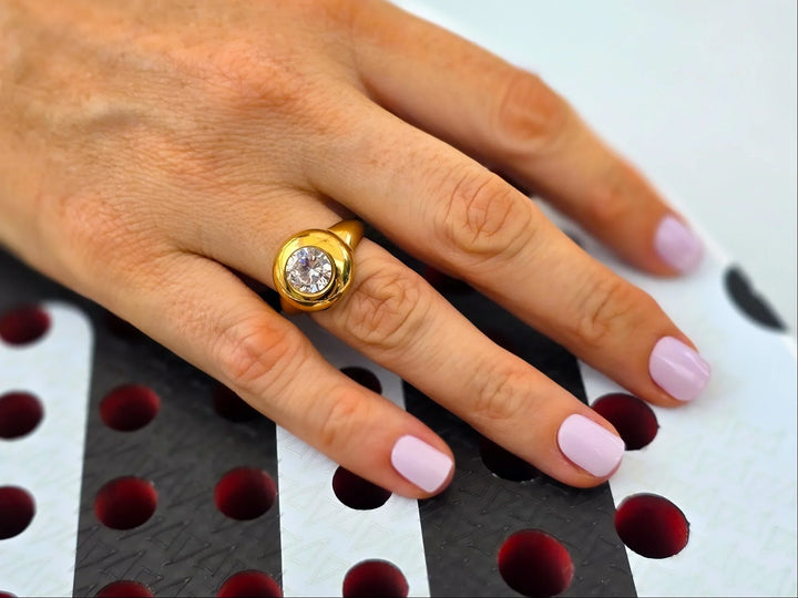 Hand wearing a gold ring with a diamond on a patterned surface