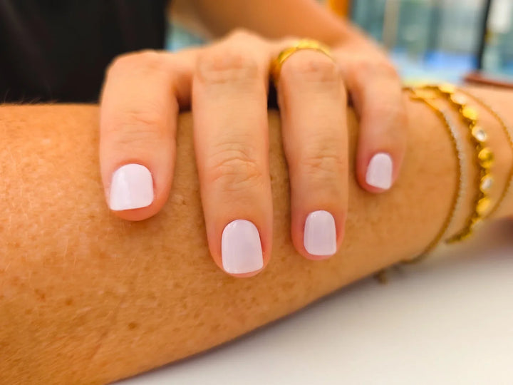 Close-up of a person's hand with pink nail polish and gold bracelets on a blurred background