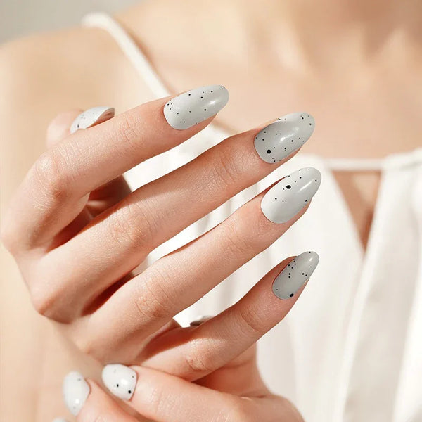 Hands with Gray Speckled Eggs gel nail wraps in pale grey, speckled with black flecks and finished with a smooth, glossy shine.