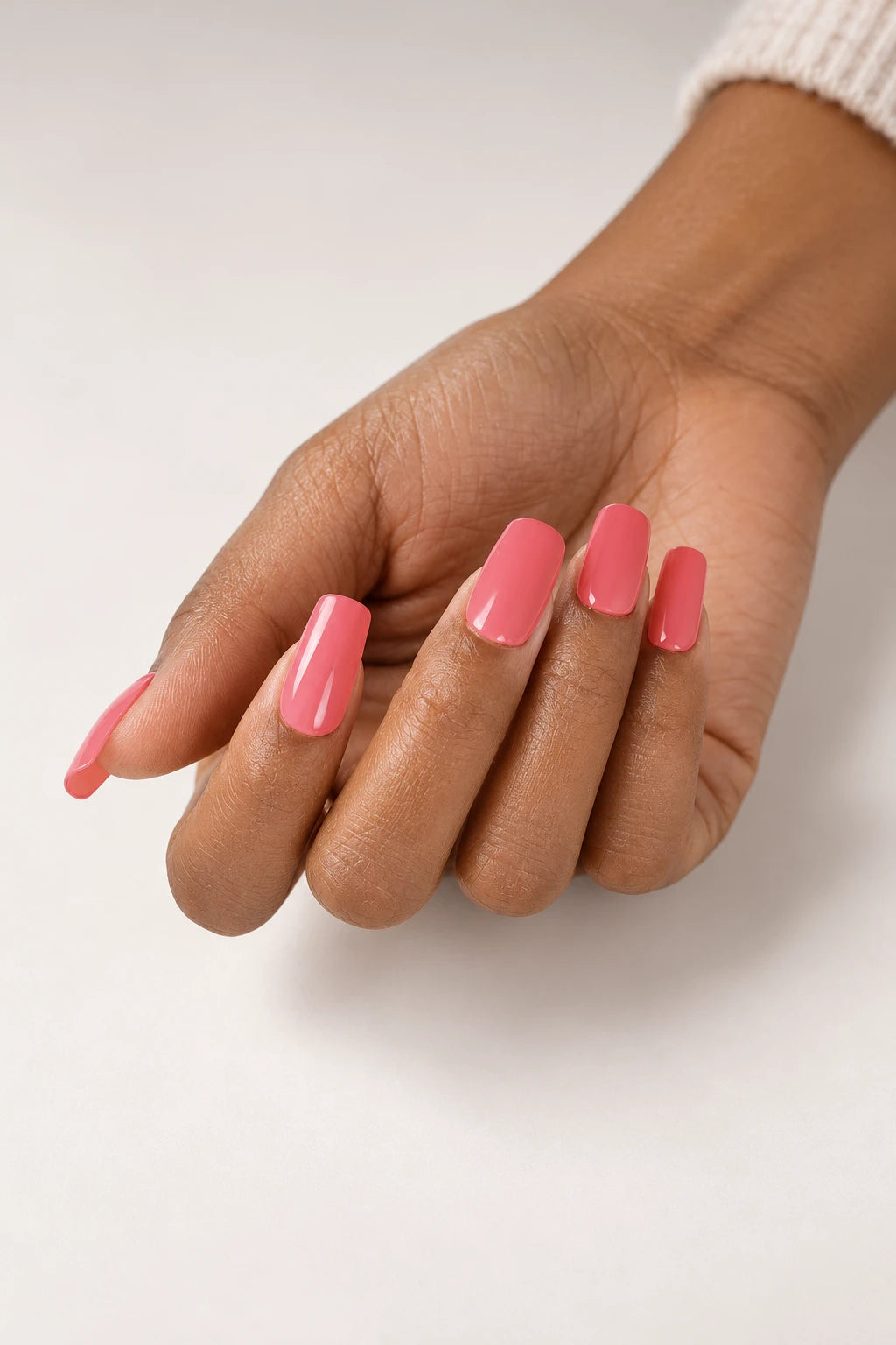 UV-free gel nail wraps in Guava, a glossy warm coral pink, shown on medium-brown skin against a soft cream background.