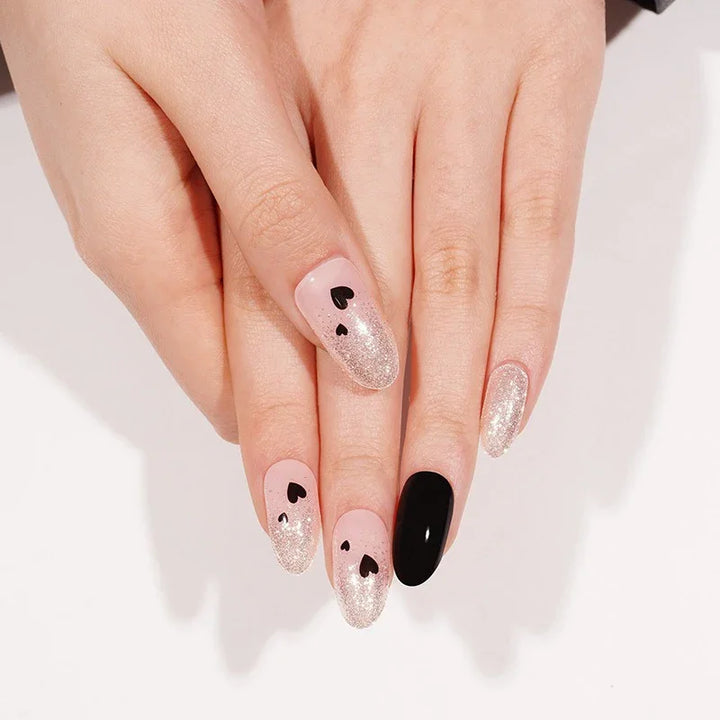 Close-up of hands with It Girl gel nail stickers in glossy pink-nude tones and black heart nail art, highlighting the contrasting black accent nails.