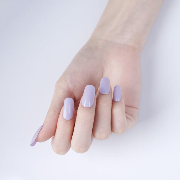 Pastel lilac stick-on gel nails with smooth glossy finish on light skin tone, photographed in soft lighting.