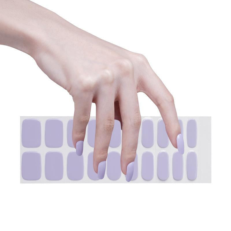 Sheet of pastel lilac semi-cured gel nail strips with high-gloss finish on light skin tone, photographed under bright  light.