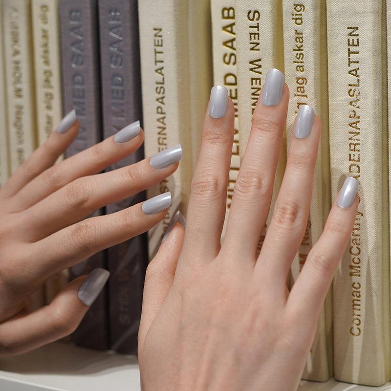 Metallic silver gel nail wraps with cool tone and glossy mirror finish on light skin tone, styled against a bookshelf in soft indoor light.