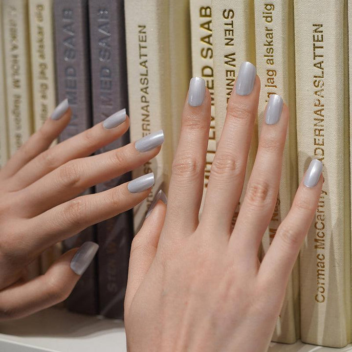 Metallic silver gel nail wraps with cool tone and glossy mirror finish on light skin tone, styled against a bookshelf in soft indoor light.