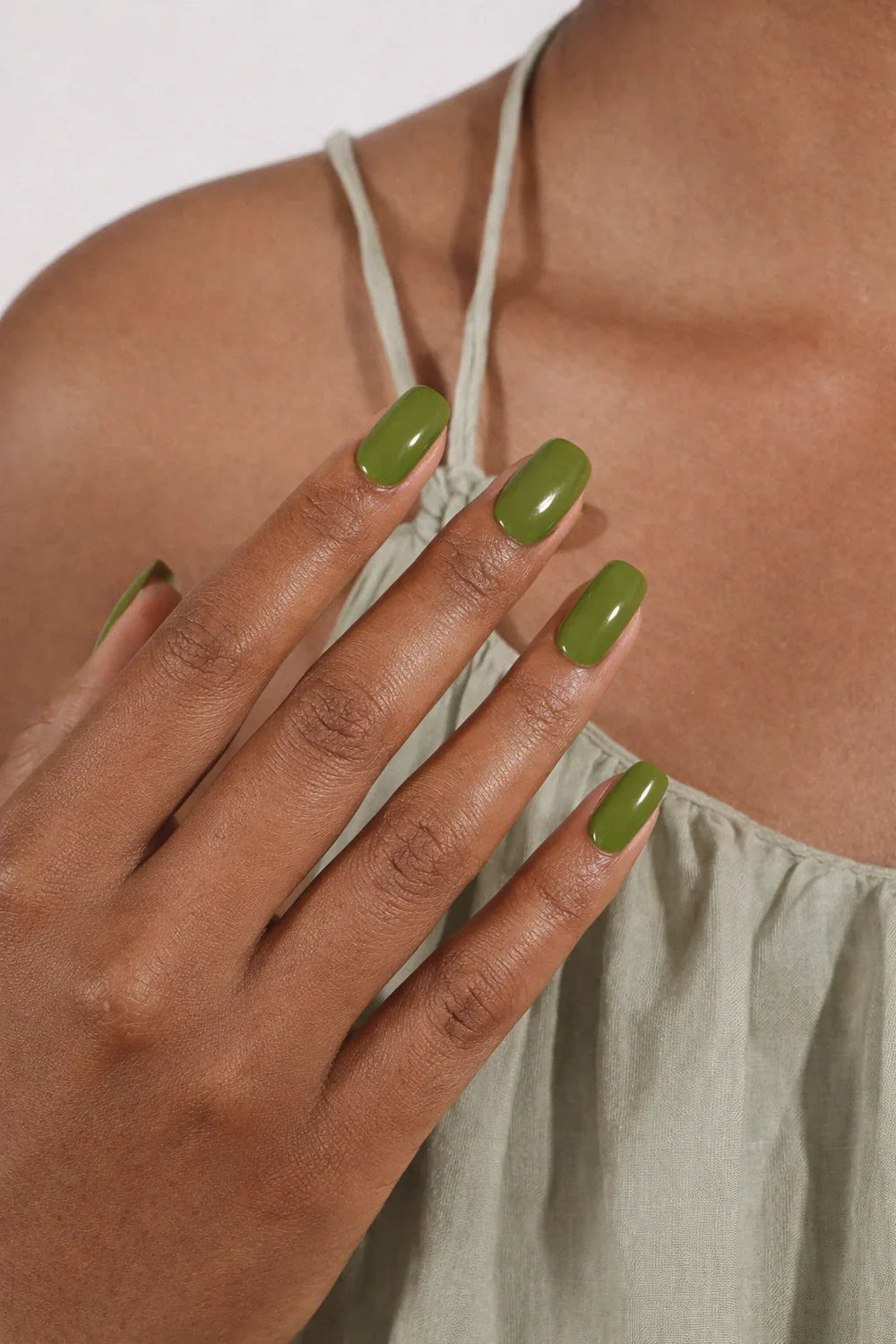 Semi-cured gel nail wraps in deep olive green with a bold, glossy finish, shown on medium-dark skin wearing a sage satin dress.