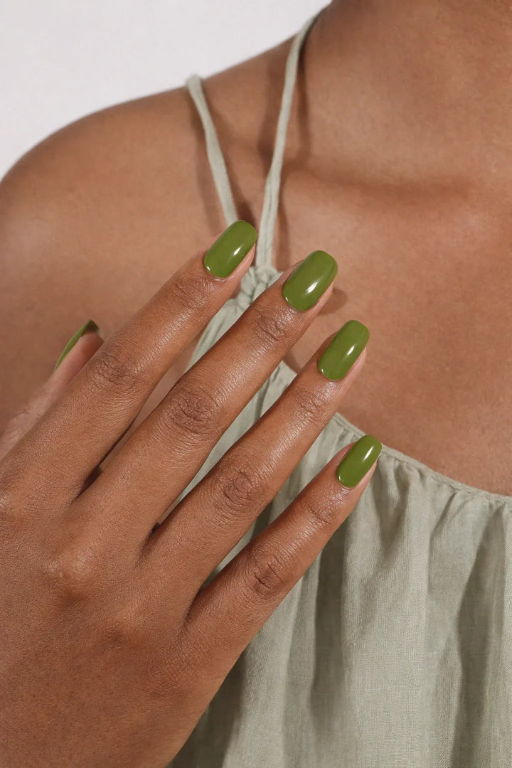 Semi-cured gel nail wraps in deep olive green with a bold, glossy finish, shown on medium-dark skin wearing a sage satin dress.