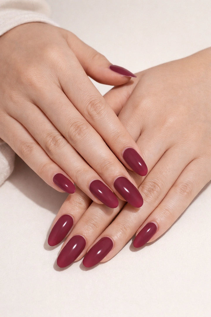 Oxblood red semi-cured gel nail stickers, shown on light skin with a deep cool-toned red shade and a smooth high-gloss finish, photographed under soft studio lighting against a neutral beige background.