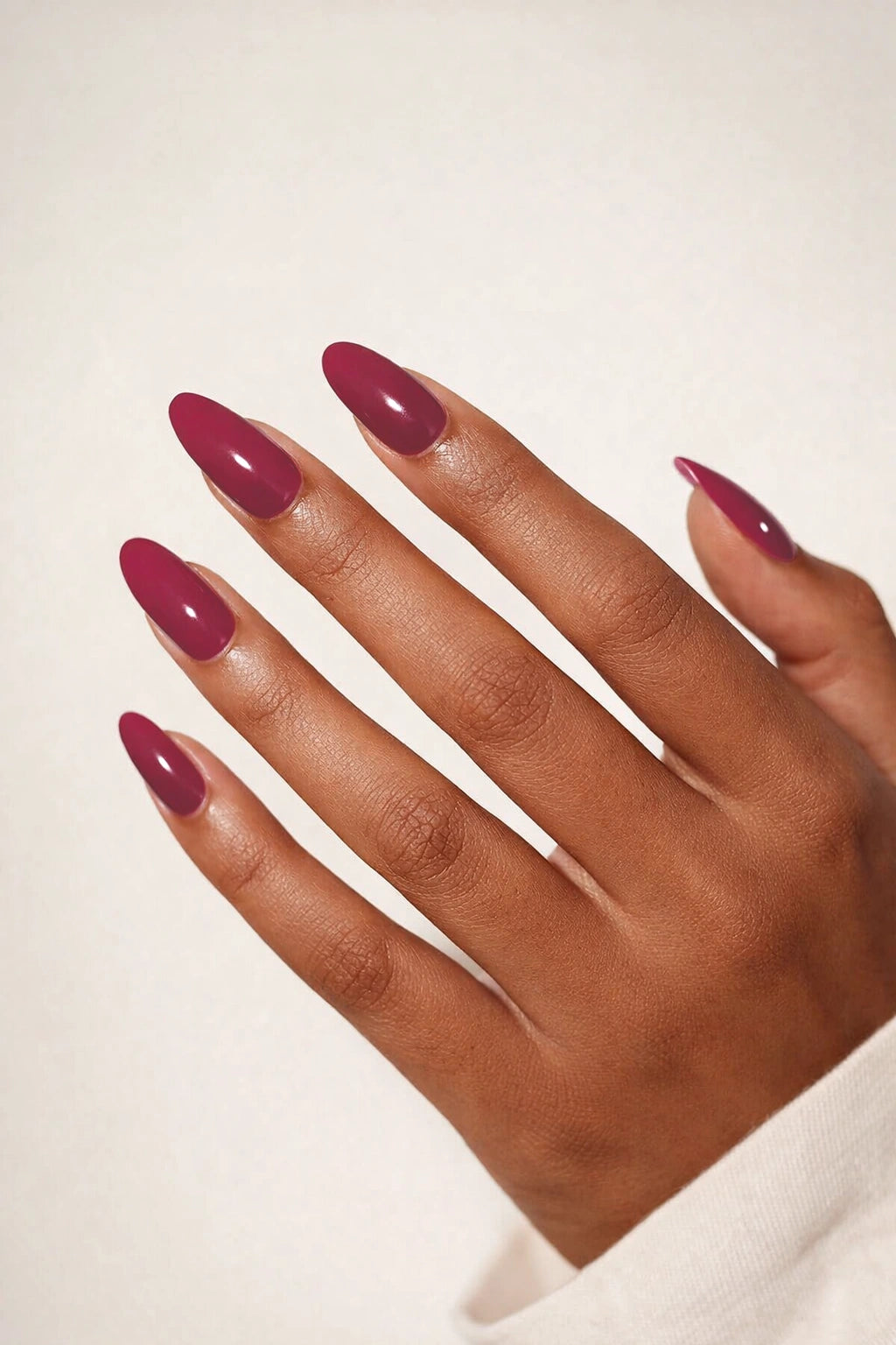 Oxblood red semi-cured gel nail stickers, shown on medium-deep brown skin with a deep blood-red shade and a smooth high-gloss finish, photographed under soft studio lighting against a clean white background.