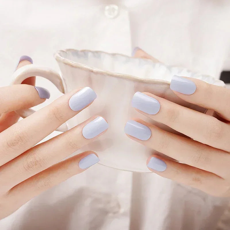Semi-cured gel nail wraps in pastel periwinkle with a glossy sheen, shown on light skin while holding a ceramic cup in natural indoor light.