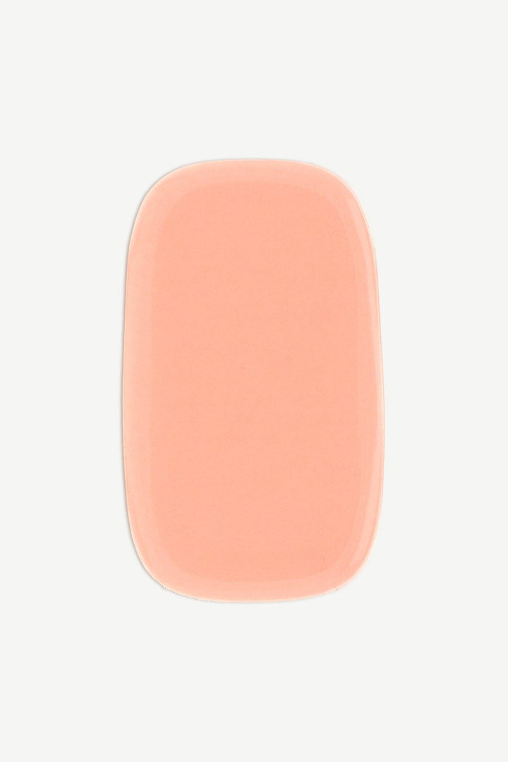 A macro image of a perfect peach stick-on gel nail strip showing a smooth, semi-transparent texture and high-gloss shine.