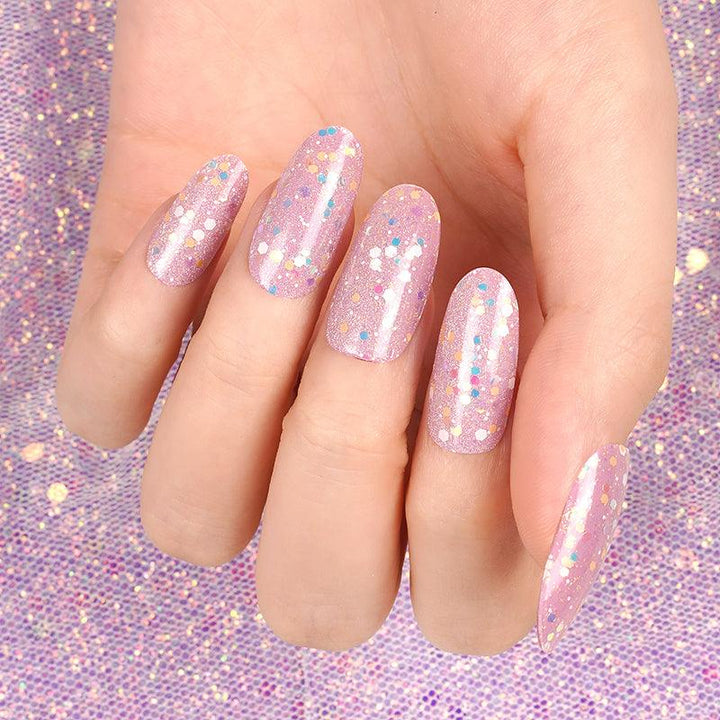 Hand with long pink glitter gel nails under bright light, showing glossy shimmer and iridescent sparkle.